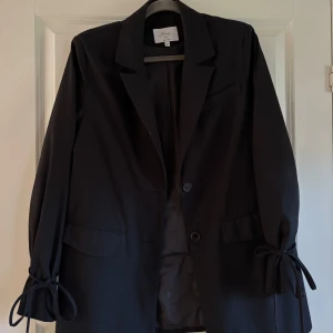 Kavaj Hanna Schönberg - Svart kavaj med knytdetalj i ärm i storlek 36. Superfint skick . Från hanna schönbergs kollektion med NA-Kd