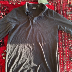 Svart pikétröja från Only & Sons, Helt ny - Säljer en svart pikétröja från Only & Sons med klassisk krage och två knappar vid halsen. Tröjan har lång ärm och är tillverkad i ett mjukt material som passar perfekt till vardags. 