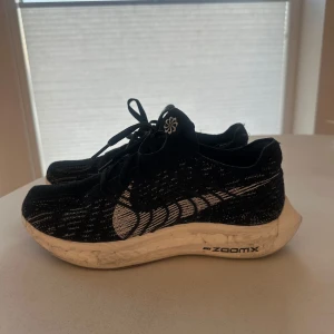 Nike pegasus - Säljer ett par svarta Nike löparskor med vit sula och tydlig ZoomX-dämpning. Skorna har snörning och ett stickat mönster i svart och vitt på ovandelen. Perfekta för dig som gillar att springa eller träna.