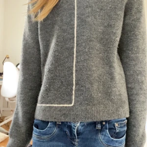 Grå stickad tröja  - Mysig grå stickad tröja från zara med en vit dekorativ linje som går från halsen och ner längs framsidan. Tröjan har rund halsringning och långa ärmar. Perfekt för kyliga dagar!