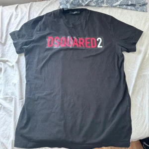 Svart t-shirt från Dsquared2 - Säljer en svart t-shirt från Dsquared2 med stor logga i rött och vitt på bröstet. Klassisk rund hals och korta ärmar. Perfekt för dig som gillar stilrena och trendiga plagg med tydlig branding. Sitter som L