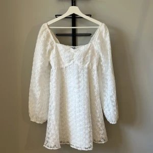 Vit studentklänning med långa ärmar - Superfin vit klänning med blommig spets och långa puffärmar. Lätt utsvängd nertill. Perfekt till studenten. Endast testad aldrig använd, prislapp kvar. 