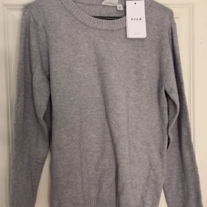 Ljusgrå stickad tröja från VILA - Säljer en ljusgrå stickad tröja från VILA. Tröjan har rund halsringning, långa ärmar och ribbade muddar vid ärmslutet. Enkel att matcha med olika outfits. Den är aldrig använd 