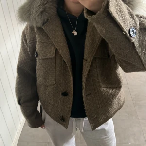 Brun ulljacka med fuskpäls från Meotine - Säljer nu min fina bruna jacka från Meotine, eftersom den inte  kommer till användning något mer. Den är i ganska bra skick förutom att knappen nere på jackan har lossnat lite och att den är lite nopprig men inget man lägger märke till. Perfekt nu inför våren och sommaren💕