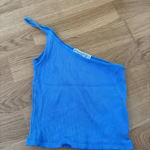 Blå ribbad oneshoulder topp - Snygg blå ribbad topp med oneshoulder-design och smal axelrem. Perfekt för att skapa en trendig look med enkel stil. Mjuk och stretchig känsla.