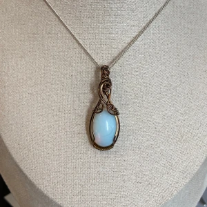 Handgjord berlock med ”opalit” och bronsfärgad tråd - Unikt halsband med en droppformad, ljusblå opal infattad i konstnärligt snirklad bronsfärgad tråd. Perfekt för dig som gillar bohemiska och eleganta smycken. Nickelfri. Kedjan ingår inte i priset.
