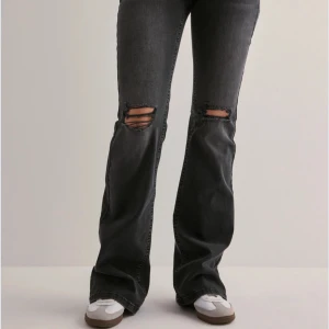 Svarta bootcut jeans med slitningar - Säljer ett par svarta bootcut jeans med slitna detaljer över knäna och broderad bakficka. Jeansen har normal passform och är tillverkade i denim. Perfekta för dig som gillar en avslappnad men trendig look. 