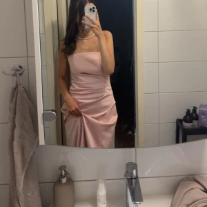 rosa balklänning - Säljer en elegant ljusrosa långklänning med smala axelband och pärldetaljer på överdelen. Klänningen har en figurnära passform och slät, glansig yta som ger en lyxig känsla. Perfekt för bal eller festliga tillfällen.