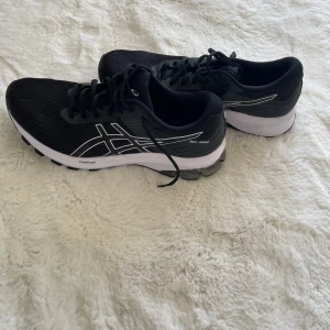 Svarta löparskor / Träningsskor - Säljer ett par svarta Asics löparskor med vita detaljer och logga på sidan. Skorna är endast testade och aldrig använda. Perfekta för träning eller löpning.