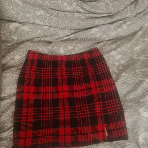 Röd och svart rutig kjol - Säljer en snygg röd och svart rutig kortkjol i klassiskt mönster. Kjolen är tillverkad i stretchigt material med 97% polyester och 3% spandex, vilket gör den bekväm och följsam. Perfekt för dig som vill sticka ut med en trendig look.