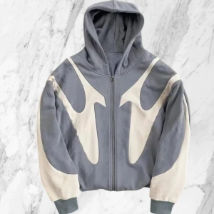 Grå hoodie med vitt mönster - Säljer en grå hoodie med dragkedja och unikt vitt grafiskt mönster på både fram- och baksida. Tröjan har huva och muddar i ärmslut och nederkant. Perfekt för dig som vill sticka ut med en cool streetwear-look.