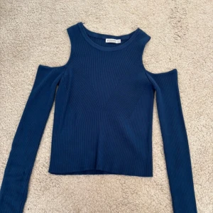 Mörkblå ribbad topp med cut-out axlar - Trendig mörkblå långärmad topp med ribbad struktur och snygga cut-out detaljer vid axlarna. Toppen har en tight passform och är perfekt för att skapa en cool och stilren look. 