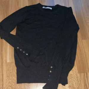 Mörkgrå tröja med knappar från Zara - Säljer en mörkgrå långärmad tröja från Zara med guld detaljer på ärmana. 