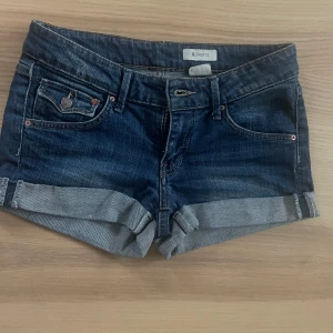 Mörkblå jeansshorts med låg midja  - Snygga mörkblå jeansshorts med upprullad kant. Shortsen har låg midja och är i en normal passform. Perfekta till sommaren och lätta att matcha med olika toppar.
