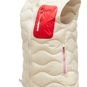 Gul dunväst med röd ficka - Stilren gul dunväst med vågigt quiltat mönster och en  röd bröstficka med dragkedja. Västen har hel dragkedja framtill och två sidofickor med ljusrosa dragkedjor. Perfekt för lager-på-lager och en sportig look. Helt oanvänd! 