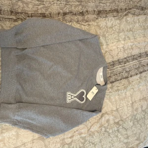 Grå sweatshirt från Ami Paris - Säljer en stilren grå sweatshirt från Ami Paris med ett stort vitt hjärta och bokstaven A broderat på bröstet.  Pris kan diskuteras!!
