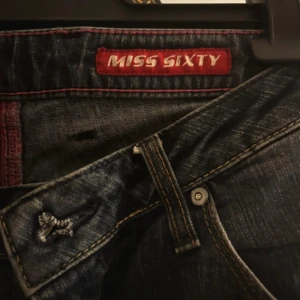 Mörkblå jeans från Miss Sixty - Säljer ett par mörkblå jeans från Miss Sixty med klassisk femficksdesign och snygga kontrastsömmar. Jeansen har normal passform  perfekt för en stilren look. Miss Sixty-logga syns tydligt i linningen.