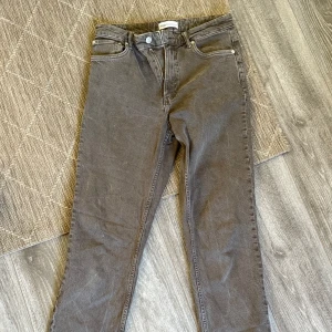 Grå jeansbyxor från Zara - Säljer ett par brun gråa jeansbyxor från Zara med raka ben och slits längst ned.  Byxorna har normal passform. Perfekta till många olika outfits!