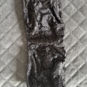 Svart spetsig tubtopp från Lindex - Säljer en svart tubtopp från Lindex i genombruten spets med blommigt mönster. Toppen är axelbandslös och har en mjuk insida för extra komfort. Perfekt för att addera en feminin touch till din outfit.