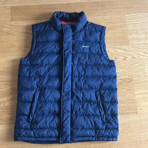 Mörkblå dunväst från Gant - En mörkblå dunväst från Gant. Inget slitage alls. Inga missfärgningar, inga revor osv. Storleken är ”176 cm” men passar som en M.