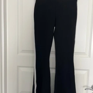Svarta bootcut byxor med vit rand från Gina Tricot - Säljer ett par svarta bootcut byxor från Gina Tricot med en vit rand längs sidorna. Byxorna har en snygg passform och är tillverkade i polyester. Perfekta för en sportig och trendig look.