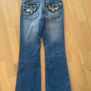 Blå bootcut jeans med coola bakfickor - Jättesnygga helt perfekta lågmidjade bootcut jeans. Dragkedjan är lite trasig men det fungerar jättebra med ståltråden. Köpta secondhand för 900kr! Midjemått rakt över är 35cm och innerbenslängd 73cm
