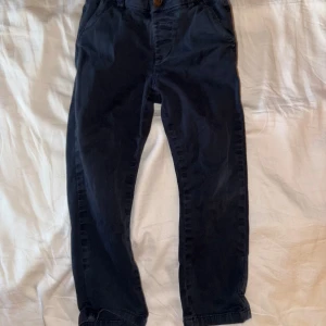 Mörkblå chinos från Next - Säljer ett par mörkblå chinos från Next med klassisk passform. Byxorna har knapp och dragkedja framtill samt justerbar resår i midjan. Perfekta för en stilren och enkel look.