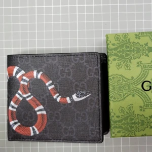 Gucci plånbok  - Säljer en svart plånbok från Gucci med GG-mönster och en röd, vit och svart orm på framsidan. Plånboken har flera kortfack och är tillverkad i skinn. Perfekt accessoar för dig som gillar lyxiga detaljer.