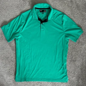 Grön golfpiké från Oakley, herr M - Säljer en grön/turkos golfpikétröja från Oakley med klassisk krage och två knappar. Tröjan är tillverkad i ett mjukt och lätt material, 