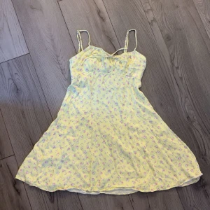 Gul blommig klänning från Zara - Söt gul klänning från Zara med små blommor i lila och rosa. Klänningen har smala axelband och en lätt utställd kjol. Perfekt för varma dagar och har en feminin, somrig känsla.