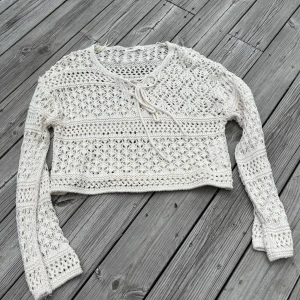 Vit virkad croppad kofta med knyt - Superfin vit virkad kofta med croppad passform och knyt framtill. Långärmad och perfekt för lager-på-lager eller som statement-plagg. Snyggt mönster och luftig känsla.
