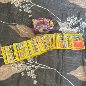Pokémon kort - Pokémon kort från 2022 Pokémon/nintendo/creatures/GAME FREAK levereras i en färgglad samlarlåda med motiv av Ash och Pikachu. Korten har gul ram och varierande motiv, perfekt för samlare eller spelare.