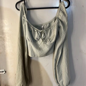 Ljusgrön topp - Supersöt ljusgrön blus från The Trend med långa puffärmar och knyt framtill. Blusen har en croppad passform och är gjord i ett lätt, strukturerat tyg som ger en trendig look.