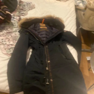 Svart vinterjacka med pälskrage från Parajumpers - Säljer en svart vinterjacka från Parajumpers med lång ärm och huva med pälskant. Jackan har dragkedja framtill och flera praktiska fickor. Perfekt för kalla dagar och riktigt snygg passform.