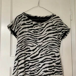 Zebramönstrad t-shirt från Second Female - Säljer en svartvit zebramönstrad t-shirt från Second Female. T-shirten har rund halsringning och korta ärmar. 