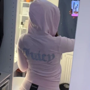 Ljusrosa hoodie från Juicy Couture - Säljer en ljusrosa hoodie från Juicy Couture med dragkedja och huva. Ikonisk Juicy-logga i glittriga bokstäver på ryggen.köpt för 1200kr💕ena metall saken på snöret är borta men annars jätte bra skick.