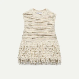 Beige stickad väst med fransar från Zara - Säljer en beige stickad väst från Zara med snygga fransdetaljer nedtill. Västen har en grovstickad struktur och är ärmlös, perfekt för att ge outfiten en bohemisk touch.