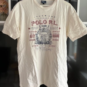 Vit t-shirt med tryck från Polo Ralph Lauren - Vit t-shirt från Polo Ralph Lauren med stort vintageinspirerat tryck i rött och blått framtill. Klassisk rund hals och korta ärmar. Perfekt för en avslappnad stil.