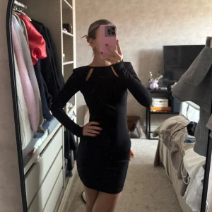 Svart långärmad klänning med öppen rygg - Säljer en svart, tight långärmad klänning med snygga cut-outs vid axlarna och en djup öppen rygg. Kort modell som sitter slimmat. Från Nakd.