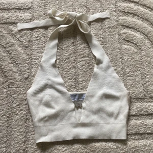 Vit ribbad halterneck topp från Bershka - Säljer en vit ribbad halterneck topp från Bershka med knyt i nacken och en dekorativ silverfärgad fjäril framtill. Toppen är croppad och har en djup v-ringning. Säljer pågrund av för liten för mig
