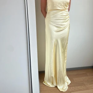 Ljusgul långklänning i satin från Stories - Säljer en elegant ljusgul långklänning i satin från Stories. Klänningen har oneshoulder-design och vacker drapering i midjan som ger en smickrande siluett. Jag är 175 cm lång och bilderna är utan klackar. Aldrig använd. Nypris: 1900 kr 