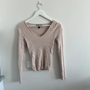 Beige ribbad v-ringad tröja - Säljer en beige långärmad tröja från New yorker med v-ringning och ribbad struktur. Tröjan har en figurnära passform och är perfekt för lager-på-lager. Enkel och stilren design som passar till mycket.