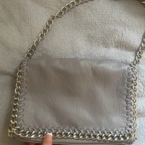 Grå axelväska med kedjedetaljer från Tiamo - Säljer en snygg grå axelväska från Tiamo. 