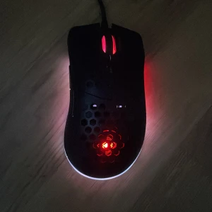 Svart gamingmus DM210 med RGB-belysning - Säljer en svart gamingmus från DM210 med RGB-belysning och honeycomb-design. Musen har två sidoknappar, DPI-knapp och röd belysning. Perfekt för gaming med låg vikt och ergonomisk form. Skriv vid minsta funderingar 😀