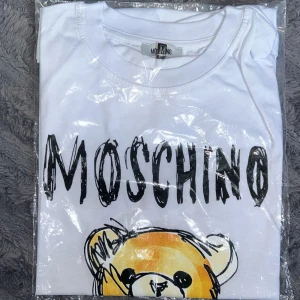 Vit t-shirt med nalletryck från Moschino - Säljer en vit t-shirt från Moschino med stort tryck av en tecknad nalle på både fram- och baksidan. T-shirten har rund hals och korta ärmar. Perfekt för dig som gillar statement-plagg och coola designer.