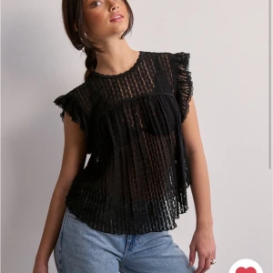 Svart blus med spets och volang - Säljer en svart blus med transparent spets och volangdetaljer vid axlarna. Blusen har korta ärmar och ett luftigt, löst fall. Perfekt för dig som gillar romantiska detaljer och vill ha en trendig topp.