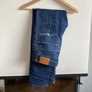 Nudie grim tim  - Säljer ett par klassiska mörkblå jeans med raka ben och kontrastsömmar. Byxorna har fem fickor. Passar perfekt till vardags och har en grisch stil.