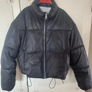 Svart pufferjacka från Bershka - Säljer en svart pufferjacka från Bershka i kortare modell med dragkedja framtill och justerbar dragsko i nederkant. Jackan har hög krage och långa ärmar, perfekt för kyligare dagar. Snygg och trendig jacka som passar till många outfits. Super fin jacka. Använd 1 vinter. Ena snöret att dra åt i midjan med har gått sönder, se bild  4🖤 annars fint skick!