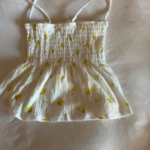 Vit  linnetopp från Gina Tricot med citroner - Supersöt vit linnetopp med smala a avtagbara axelband från Gina Tricot. Toppen har smock upptill och ett utsvängt avslut. Dekorerad med små gula citroner över hela tyget. Perfekt för varma dagar!