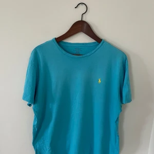 Blå t-shirt från Polo Ralph Lauren - Säljer en blå t-shirt från Polo Ralph Lauren. Skick 8/10, inga tecken på användning. Perfekt basic-plagg för garderoben. Skön och enkel att matcha till olika outfits.